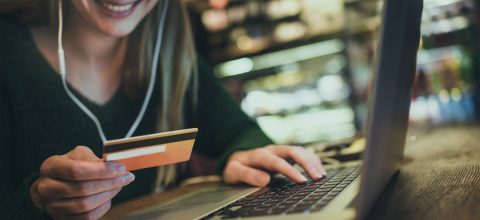 Woman on headphones is entering her credit card number into her laptop while at a café.