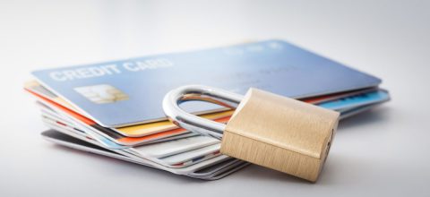 A stack of credit cards on a flat surface with a brass padlock placed on top.