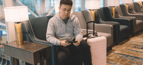 A man sitting in an airport lounge on his phone with his luggage next to him.