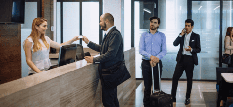 A male traveler checking in at a hotel front desk while other people wait in line.