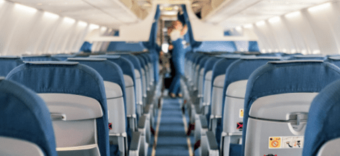 View of the interior of an airplane showing multiple empty rows and a flight attendant in the background.