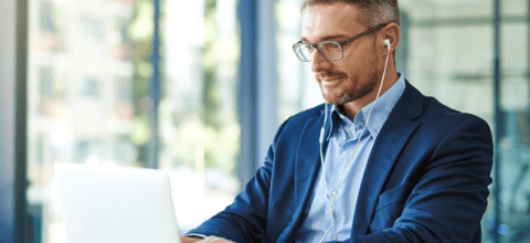 A man wearing glasses and headphones looks at a laptop screen.