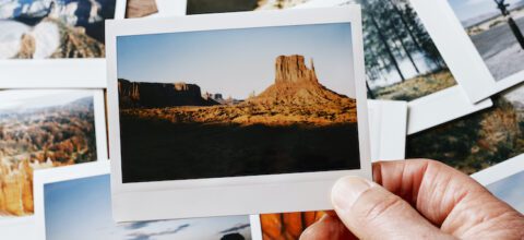 A hand holding a photo of a canyon, an various other photos in the background.